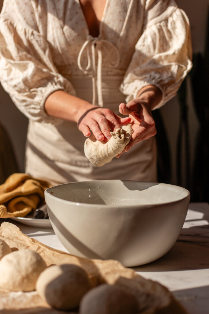 Gently shaping a piece of sourdough cottage cheese bagel dough to form a smooth round.