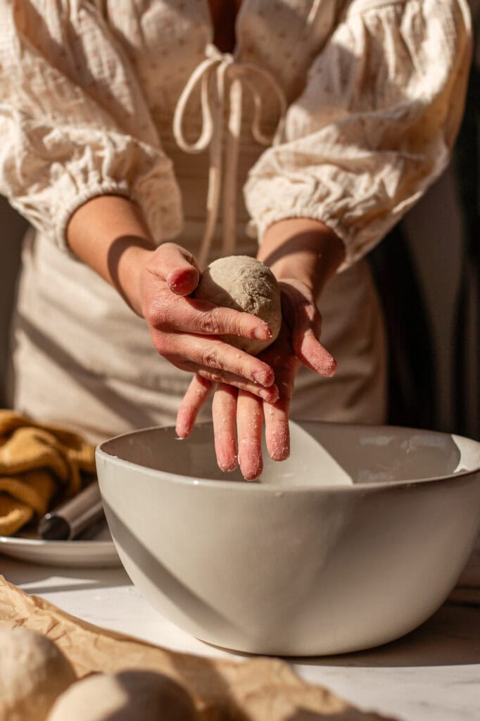 Hands holding a perfectly shaped ball of sourdough cottage cheese bagel dough.