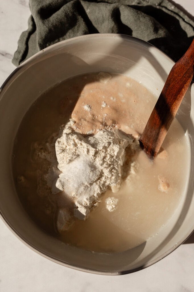 Mixing wet and dry ingredients in a bowl for sourdough bread, including water, flour, salt, and sourdough starter.