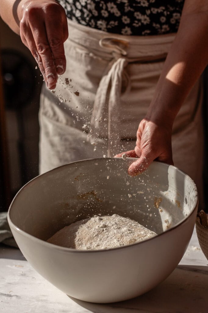 Dusting flour over the sourdough dough to prevent sticking during shaping.