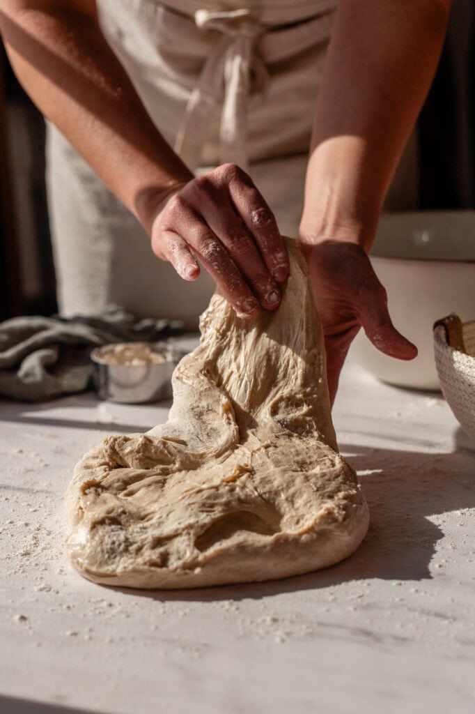 Gently stretching the sourdough dough upwards to create tension and elasticity.