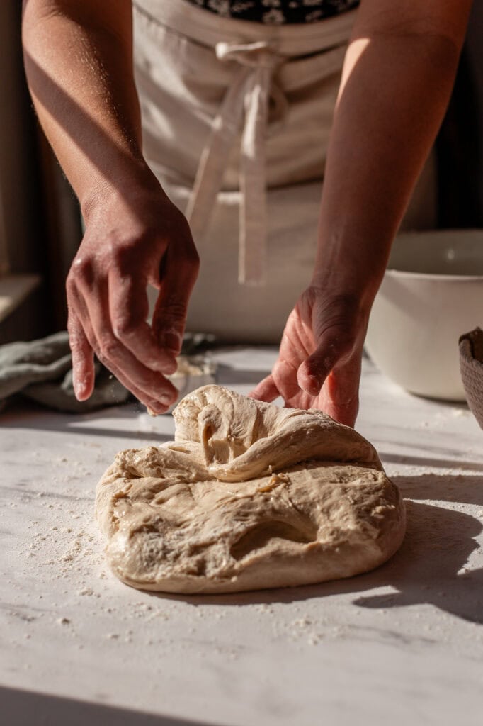 Pulling edges of sourdough dough into the center to start shaping it into a boule.