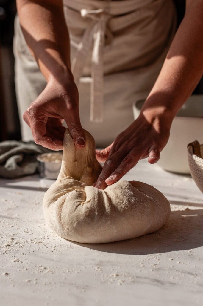 Pinching the folded seams of the sourdough dough together to seal the bottom of the boule.