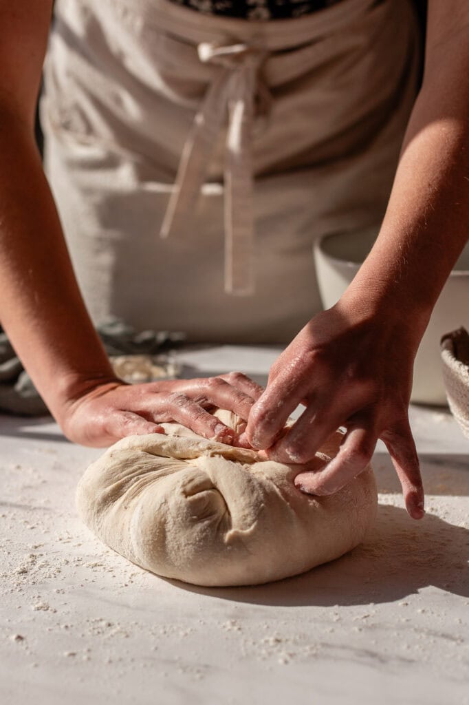 Smoothly shaping the sourdough dough into a cohesive boule, ready for the final proof.