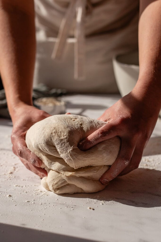 Lifting and flipping the sourdough dough to create a tight structure and enhance surface tension.