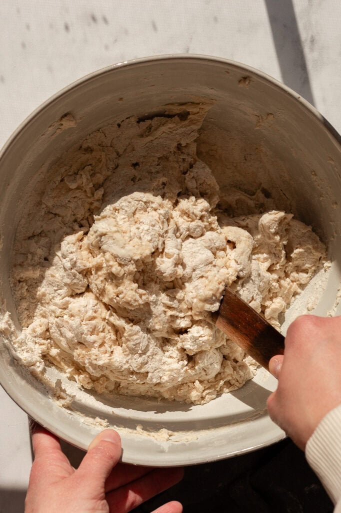 A bowl with partially mixed sourdough ingredients, showing a rough and sticky dough forming.