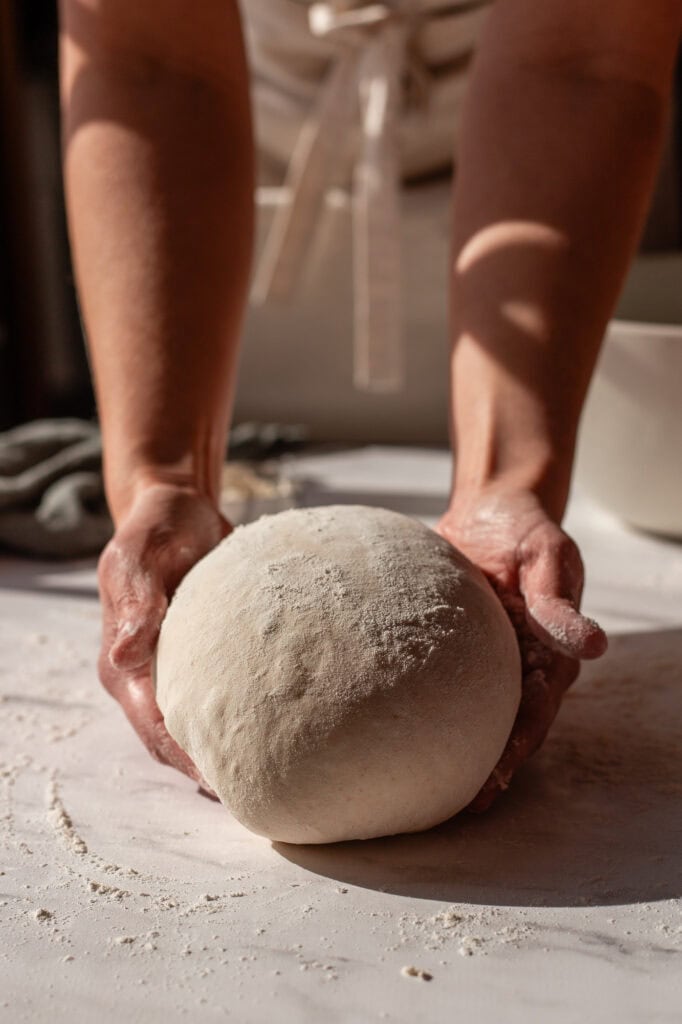 Fully formed sourdough boule resting on a floured surface, ready to be transferred to a proofing basket.