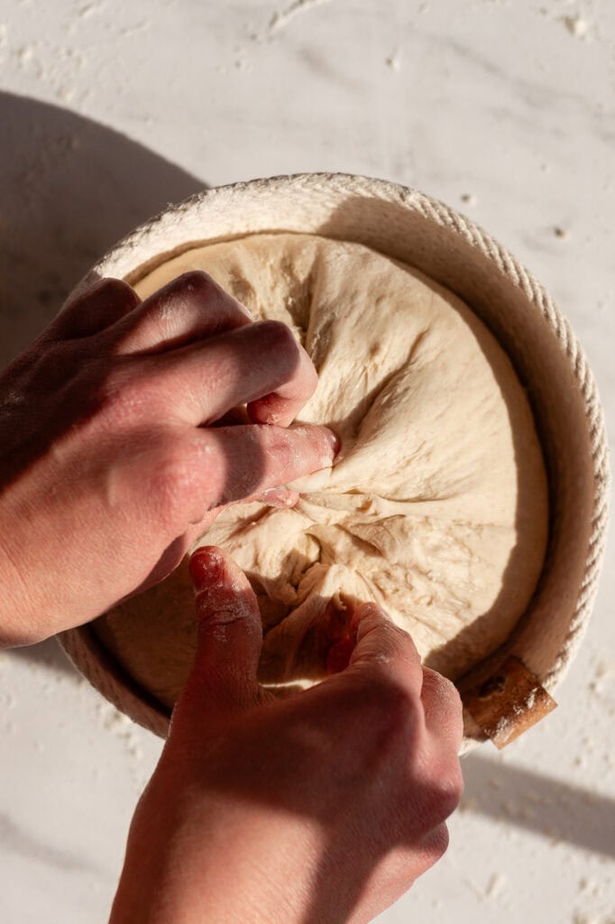 Pinching and securing the bottom of the sourdough boule to create tension before proofing.