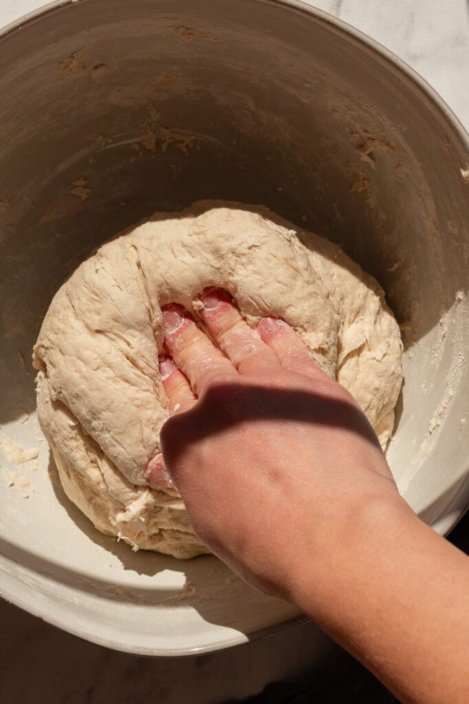 Hands kneading sourdough dough in a bowl to create a smooth consistency.