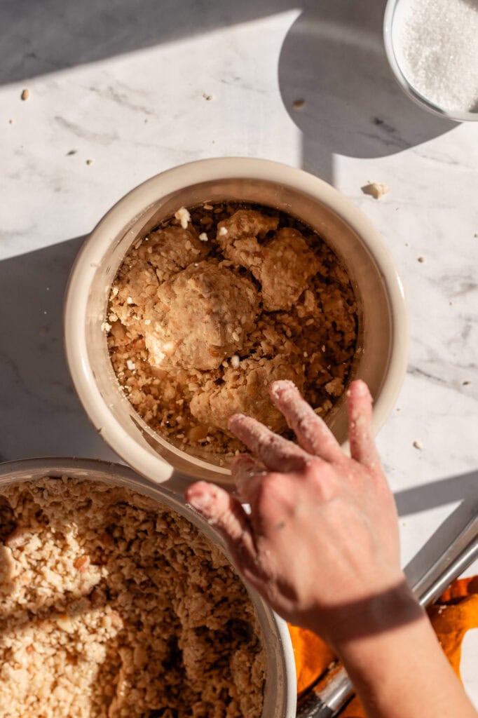 Hand releasing a miso ball into the crock, pressing it firmly to remove air bubbles and prevent mold growth. 