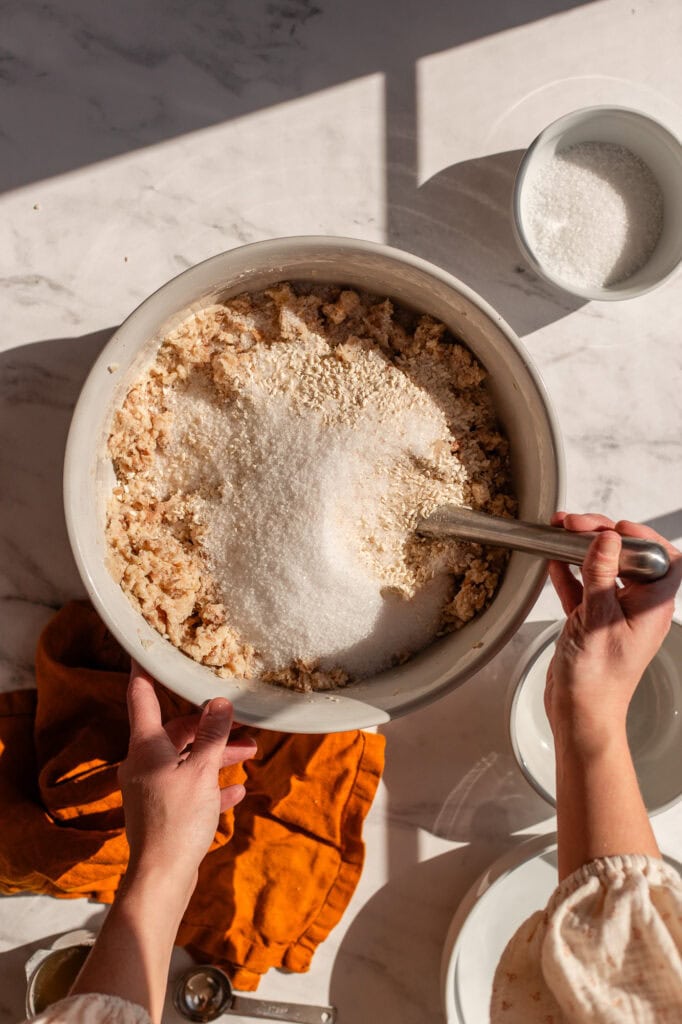 Top-down view of a large bowl filled with mashed beans and koji rice, with a layer of salt added on top, ready to be mixed. 