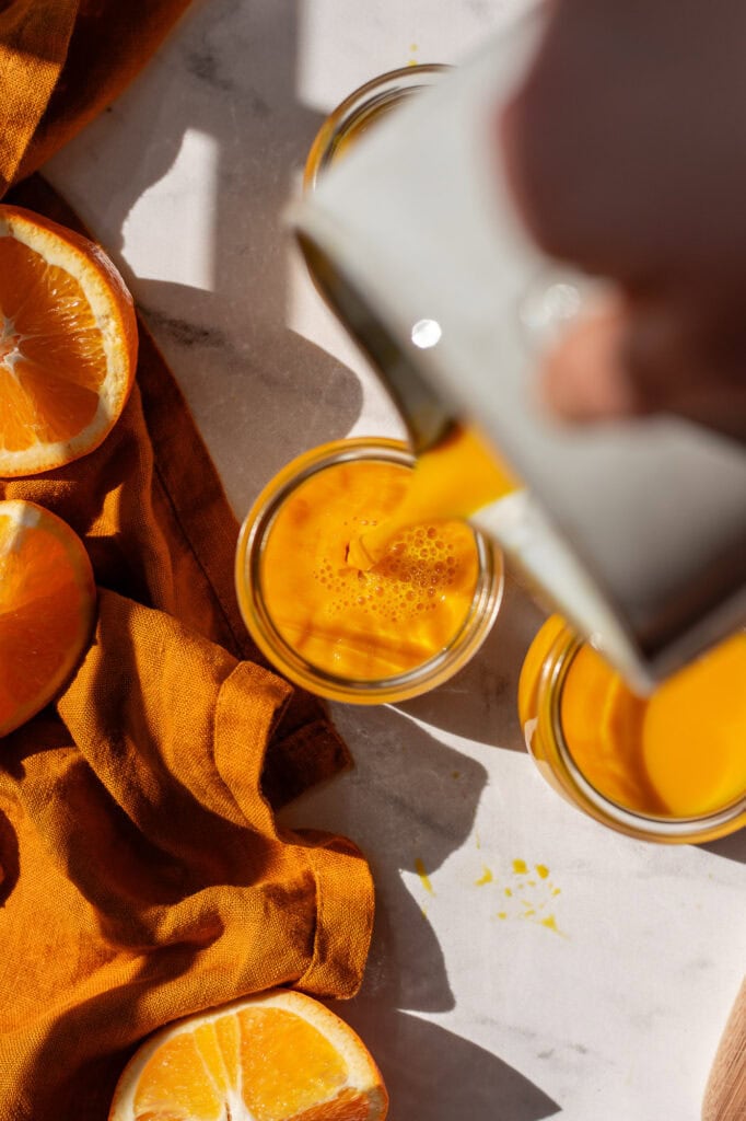 A pitcher of ginger turmeric kombucha pouring into a single serve cup.