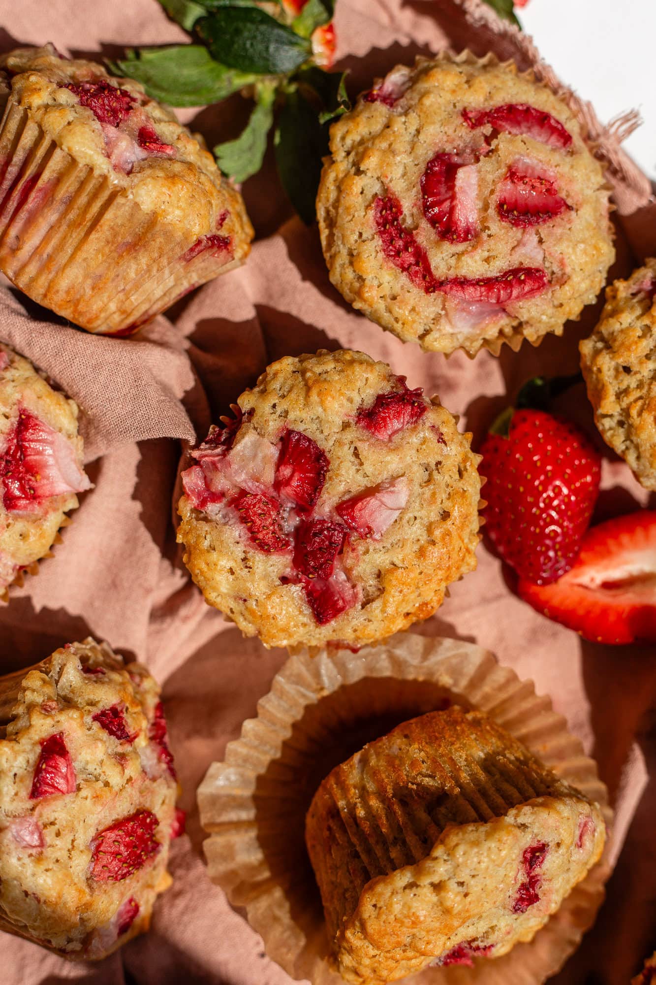 A close-up of freshly baked oatmeal strawberry muffins with sourdough discard, featuring golden-brown tops and vibrant red strawberry pieces.