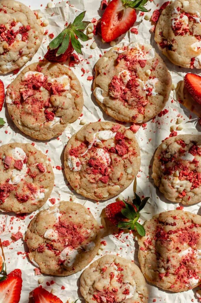 Several baked strawberry and cream cookies sit on a parchment paper lined counter. 