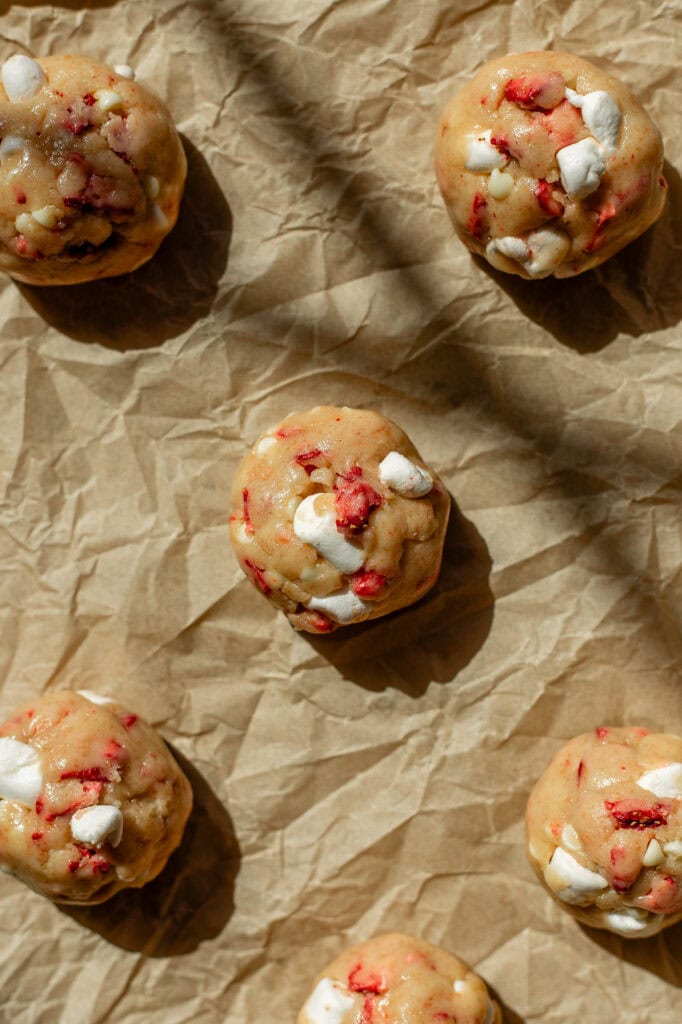 A strawberry and cream cookie dough ball sits on a pan lined with parchment paper.