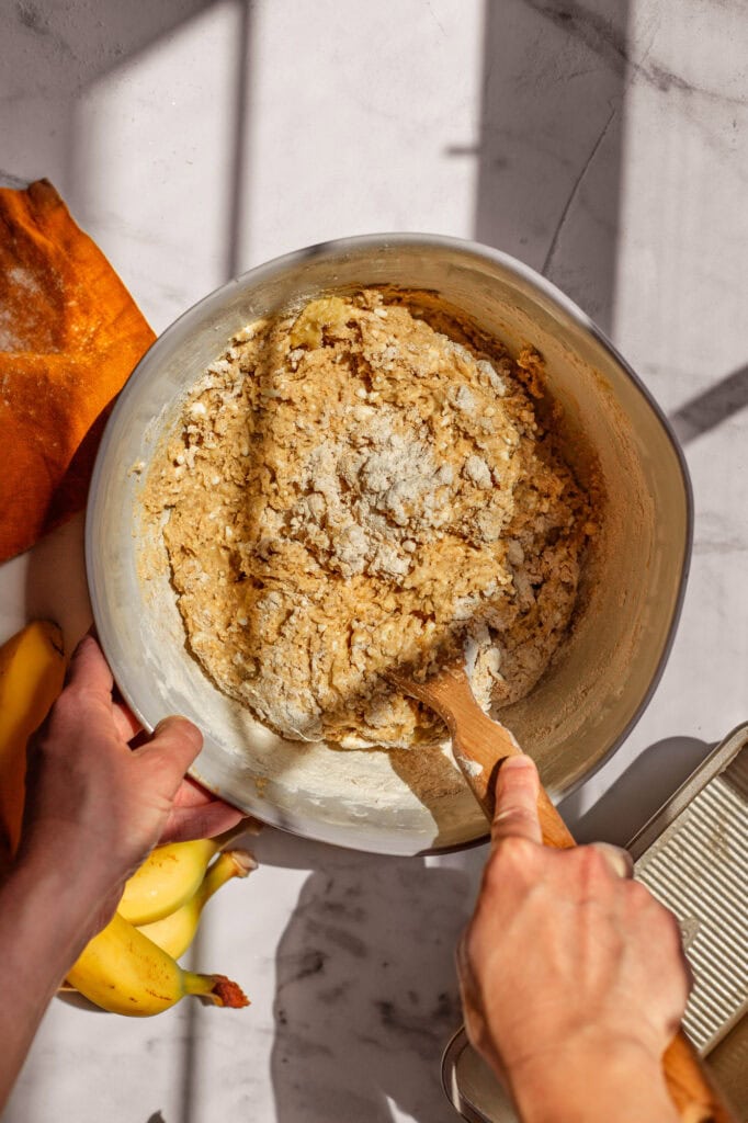 Hands mixing together cottage cheese, mashed banana, sourdough starter, eggs, and dry ingredients to make banana bread batter.