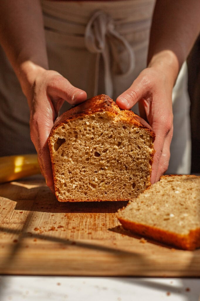hands holding the finished banana bread loaf and showcasing the texture of the bread.