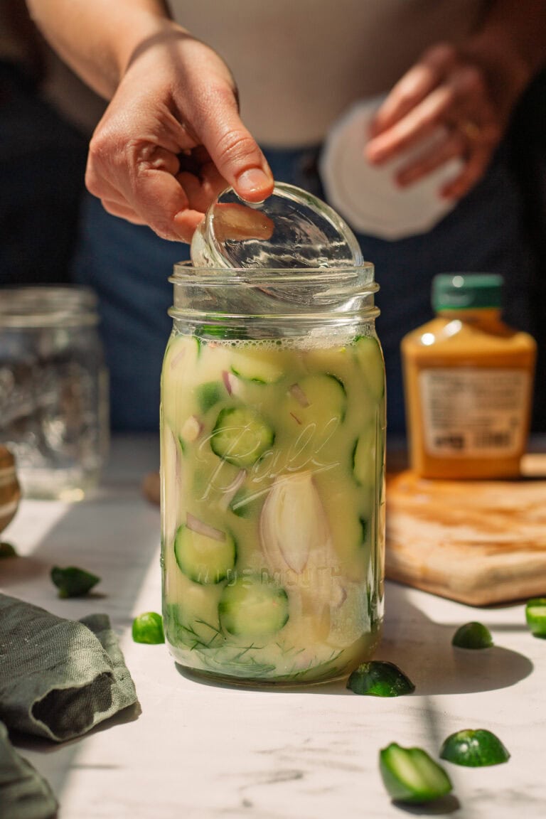 A fermentation weight is being lowered into a jar of honey mustard pickles.