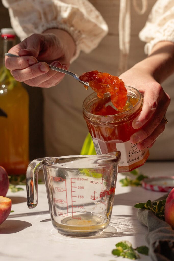 Hands scooping peach preserves into a measuring cup.