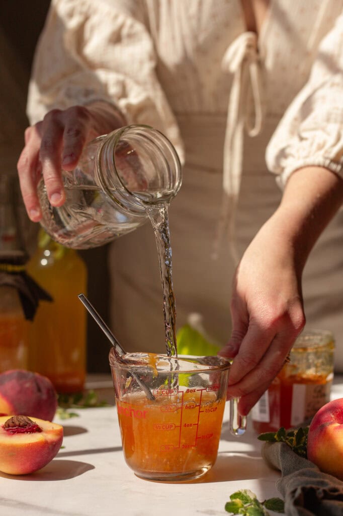 hands puring water into peach preserves to dissolve eveything.
