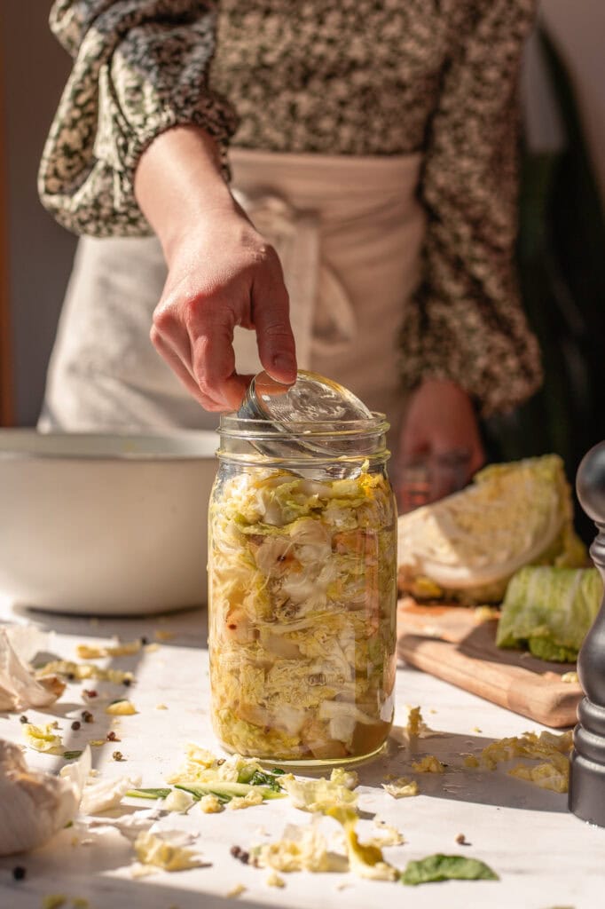 roastedgarlicsauerkrautblackpepper A woman is putting a jar of cabbage into a jar