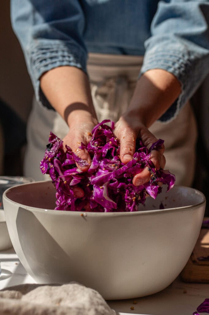 Side view of hands massaging salt into red cabbage.