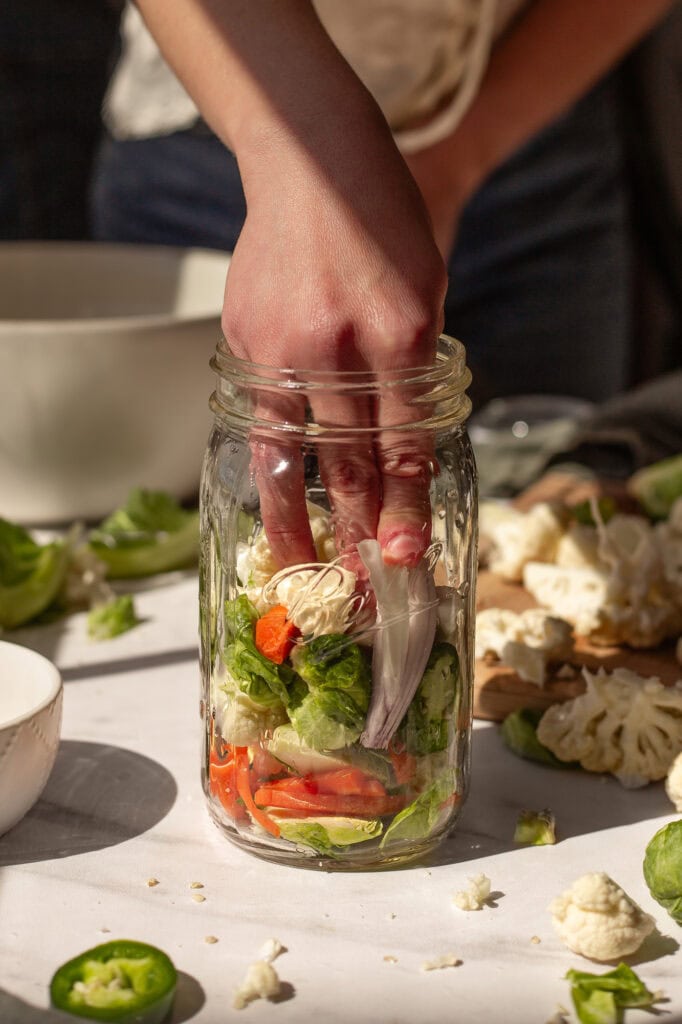 Raw giardiniera Ingredients Going into a Jar A person is putting giardiniera vegetables in a jar.