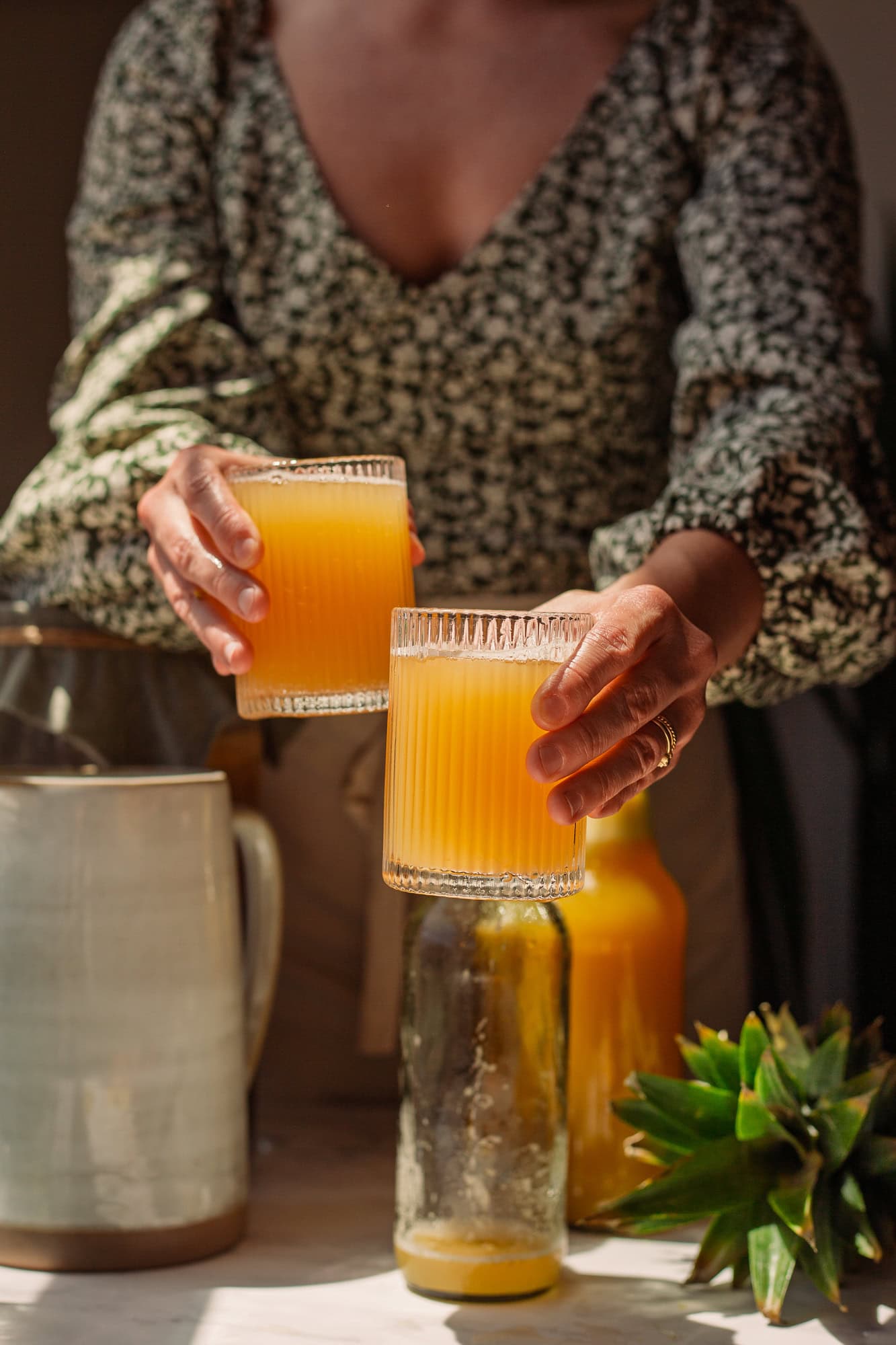 A person holding two glasses of pineapple kombucha.