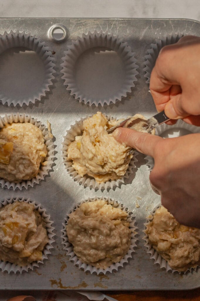 Portioning out Muffin Batter Hands use a measuring spoon to put muffin batter in a muffin tin.