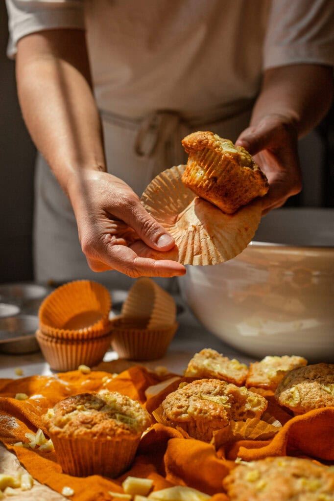 Peeling Off Muffin Wrap Hands peel off the muffin liner on a baked pineapple muffin.