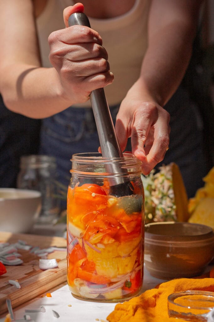 Tamping pineapple and pepper mixture into the jar to release juices.