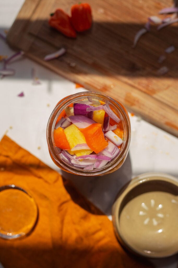 Top-down view of chopped pineapple, peppers, and onions in a jar before pressing.