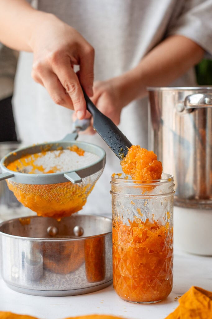 Straining pulp from blended hot sauce using a fine mesh strainer.