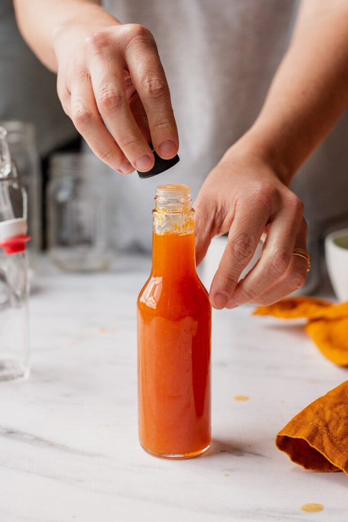 Placing a cap on a glass bottle filled with finished pineapple habanero hot sauce.