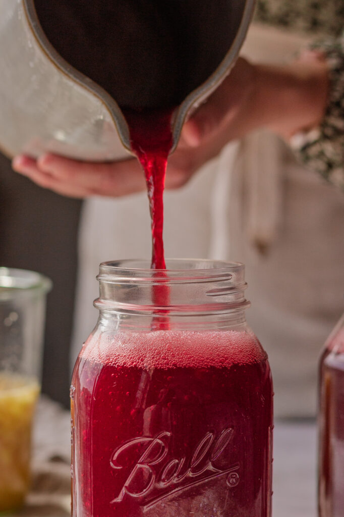 Pouring Strained Ginger Bug Drink Mix in a Mason Jar Hands pouring the strained ginger bug drink mixture into a quart sized mason jar.