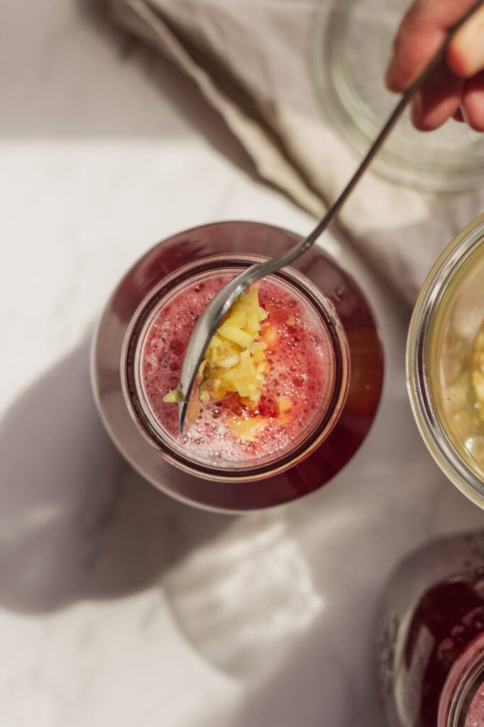Introducing Ginger Bug into Drink Mixture A top down view of the mason jar full of liquid. A spoon is introducing the ginger bug to the mixure.