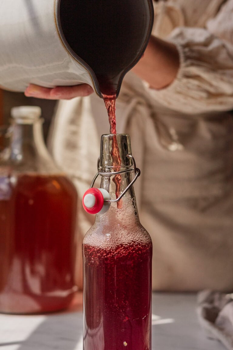 Hands pouring strained ginger bug drink into a pressure safe bottle for second fermentation.