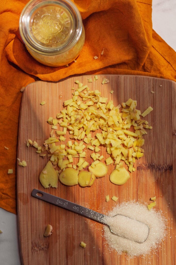 Chopped ginger and cane sugar Fresh ginger root finely chopped on a wooden cutting board, next to a spoonful of organic cane sugar.
