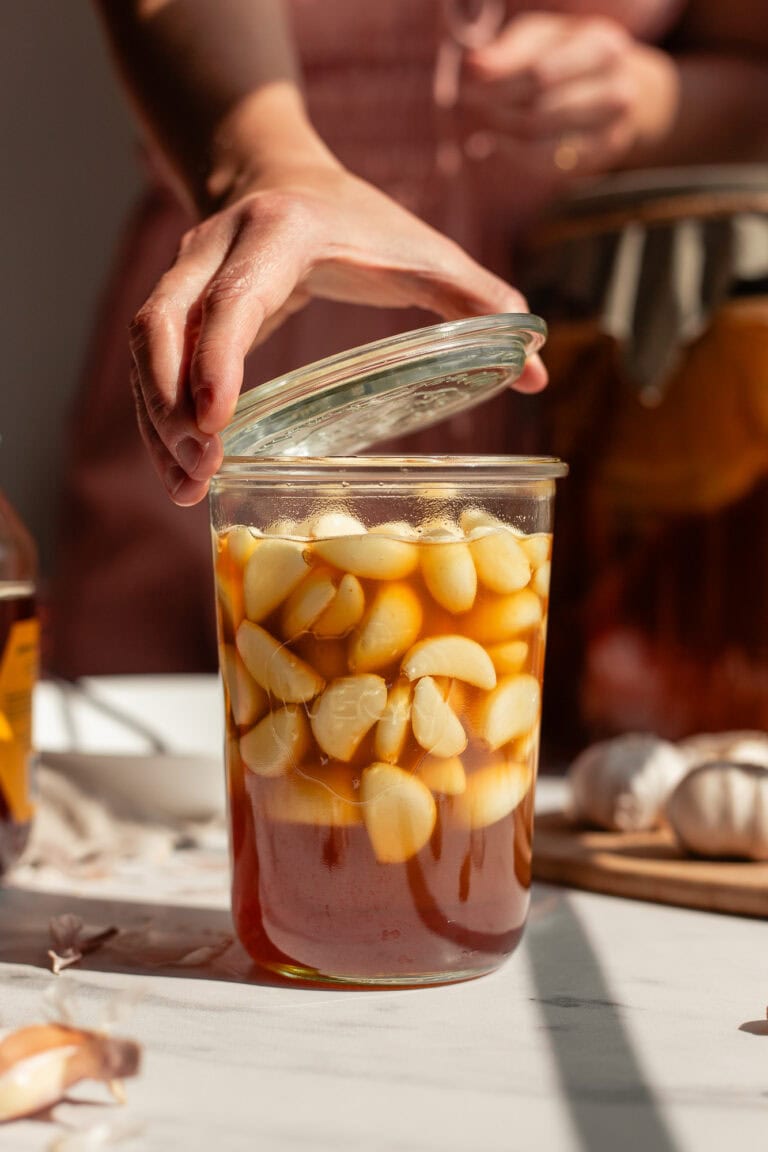 With the honey garlic oxymel filling the glass Weck jar, a hand places the lid on top.