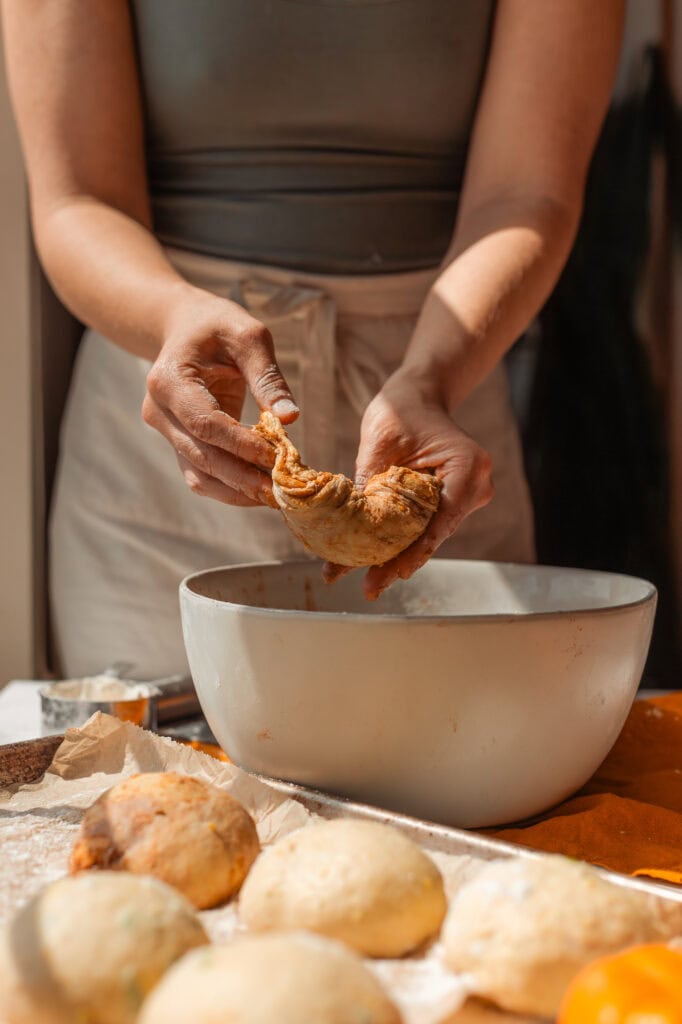 Folding the CinnamonSwirled Dough Hands gently folding and tucking a quarter portion of the pumpkin sourdough dough to develop a smooth dough ball.