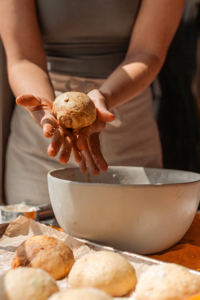 PreShaping the Cinnamon Swirl Bagel Dough Hands cupping and rolling a portion of the sweet pumpkin sourdough dough into a tight, round ball.
