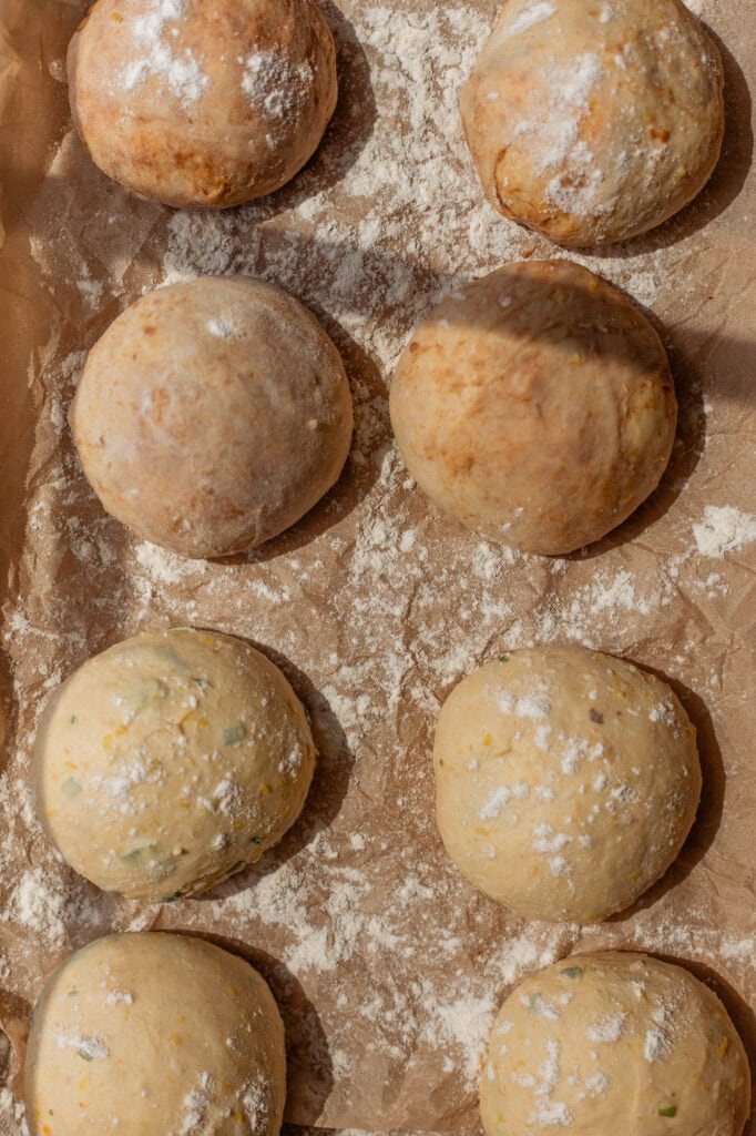 Proofing the savory and sweet dough balls Six pre-shaped balls of savory and sweet pumpkin sourdough dough, lightly dusted with flour and resting on a sheet of parchment paper on a baking sheet.