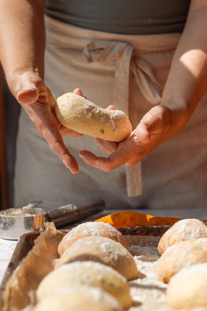 Preparing the Savory Bagel A person's hands gently rolling a savory pumpkin sourdough dough ball to elongate it into a bagel shape.