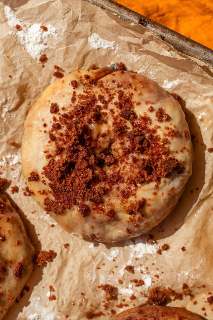 Topping the Cinnamon Swirl Bagel with Crumble A close-up of a sweet cinnamon pumpkin bagel resting on parchment paper, topped with a thick layer of brown sugar and cinnamon crumble before baking.