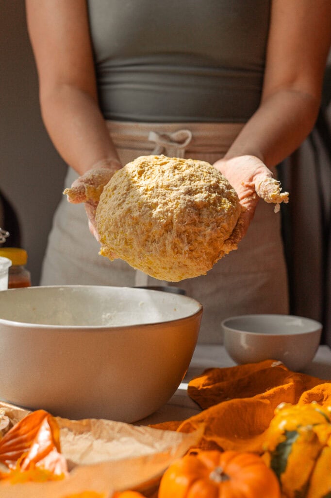 The Perfect Sourdough Pumpkin Dough Ball A round, golden-yellow ball of fully mixed pumpkin sourdough dough held with two hands, ready to be placed in a separate bowl for resting.