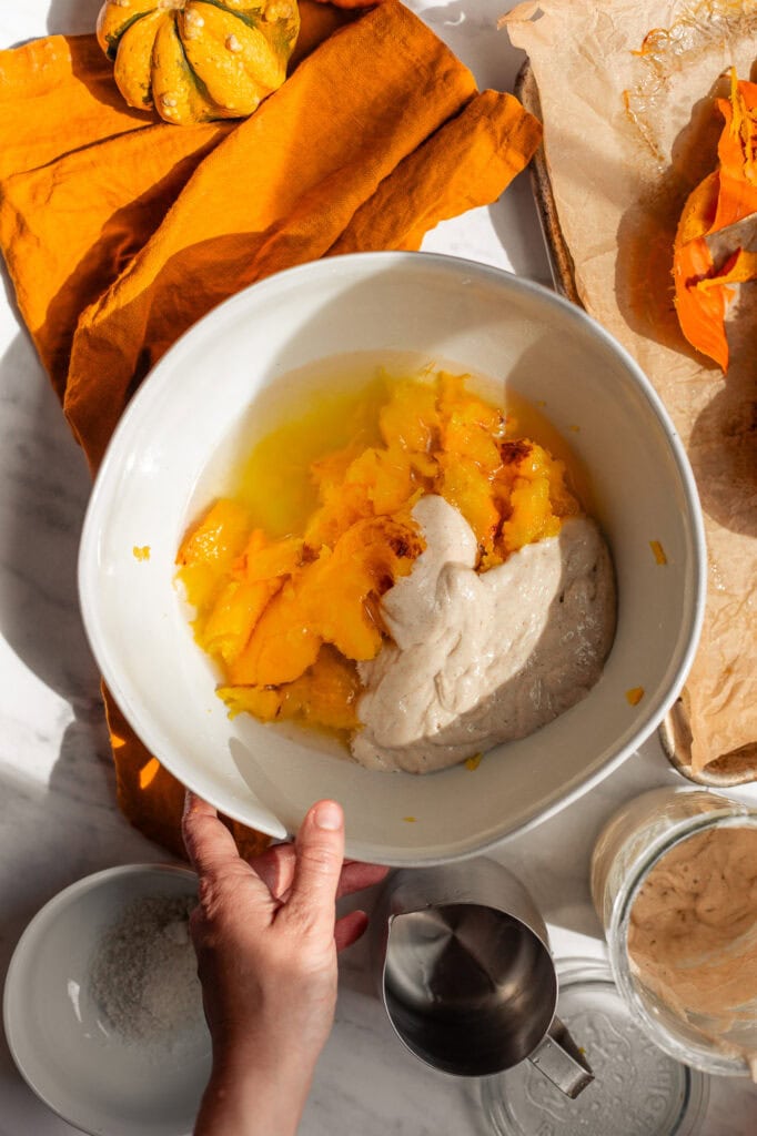 Roasted Pumpkin and Sourdough Starter A white bowl filled with bright orange roasted pumpkin, yeast, and sourdough starter.