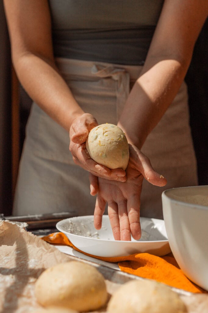 Rolling the Savory Bagel Dough into a Tight Ball Hands cupping and rolling a portion of the savory pumpkin sourdough dough on the counter to form a smooth, tight, round ball.