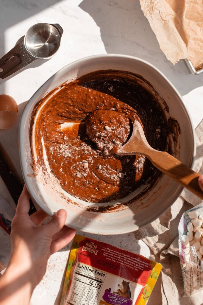 Brownie box mix is added to the ingredients mixture and mixed with a wooden whisk. 