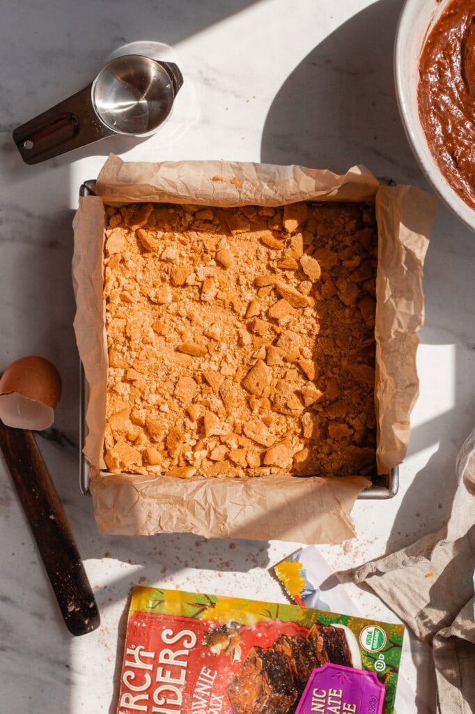 Crunchy graham cracker is crumbled as a topping on top of the brownie mix in a baking dish.