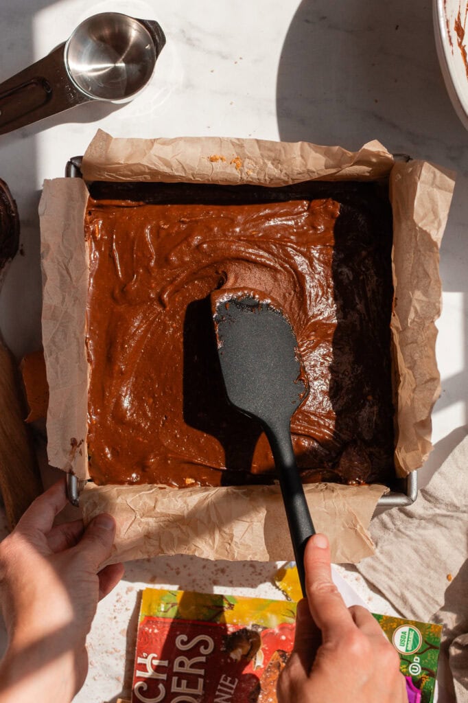 A rubber spatula spreads another layer of brownie mix atop the graham cracker crumble topping.